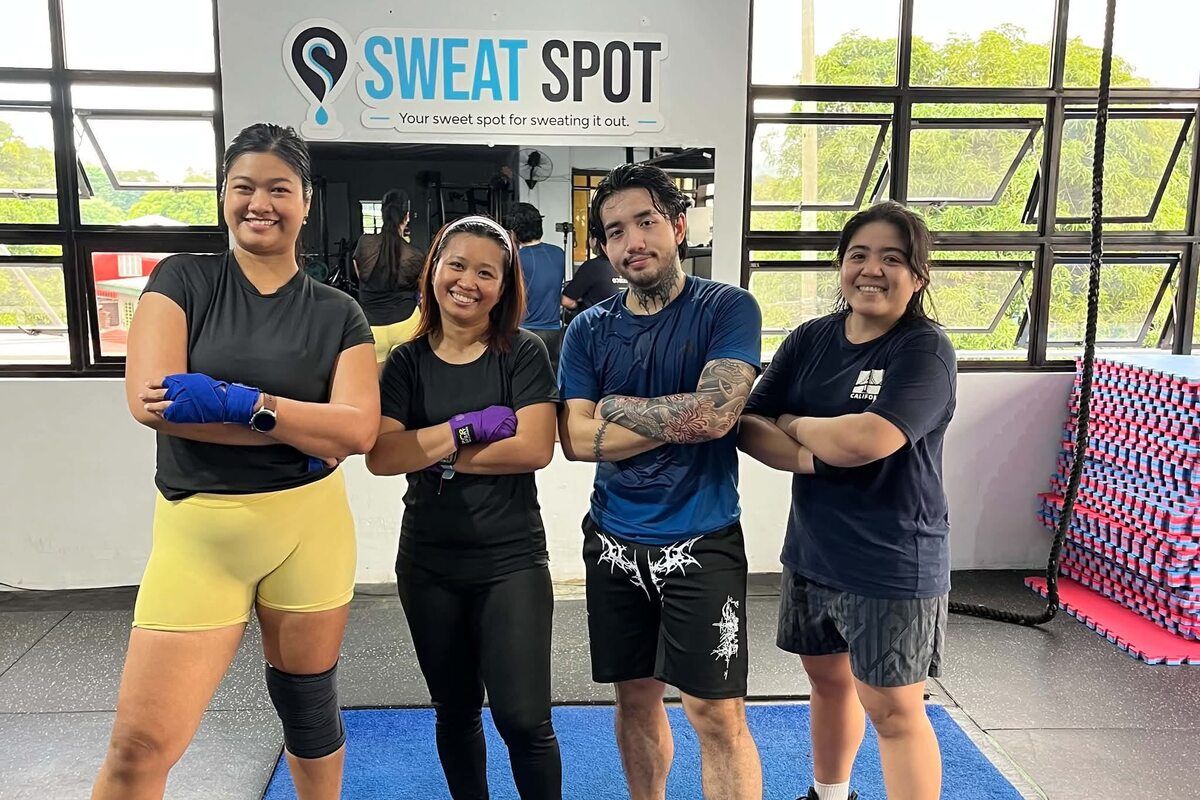 Four members posing with folded arms on the mat, two of them wearing hand wraps